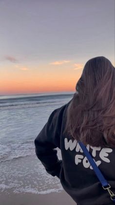 a woman standing on the beach with her back to the camera and looking at the ocean