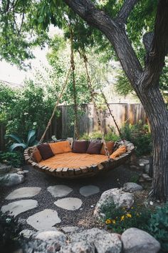 a swing bed in the middle of a garden with rocks around it and trees surrounding it