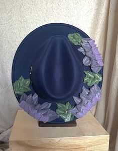 This one of a kind, hand painted, textured floral fedora is the perfect walking art piece. Each hat is uniquely crafted and perfect for any occasion.  This navy blue fedora is crafted with soft glittered purples, lavender, and green accents. These island treasures are shipped straight to you from the Hawaiian island of Oahu. (Hats are water resistant. Keep out of heavy rain. Spot clean only) Handmade Blue Fedora With Flat Brim, Handmade Blue Fedora With Curved Brim, Handmade Blue Wide Brim Fedora, Blue Fedora With Curved Brim For Festival, Artisan Blue Fedora With Short Brim, Artisan Blue Fedora With Curved Brim, Artisan Blue Hat With Flat Brim, Artisan Blue Fedora Hats, Blue Artisan Hat With Flat Brim