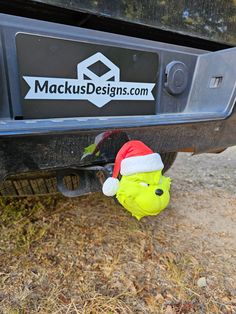 a green stuffed animal wearing a santa hat under the bumper of a vehicle with stickers on it