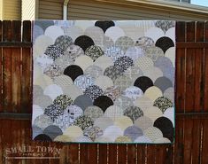 a quilt hanging on a wooden fence in front of a house with a wood fence