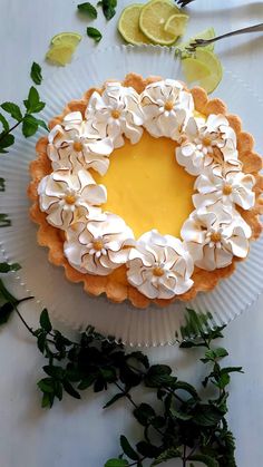 a lemon tart with white flowers and leaves on a plate next to lime wedges