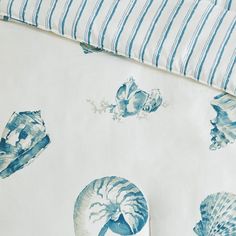 a blue and white bed spread with seashells printed on it, next to a striped pillow