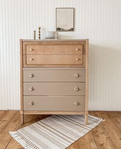 a dresser with three drawers and a rug on the floor in front of white walls