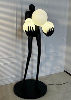 a lamp that is on top of a black stand in front of a white wall