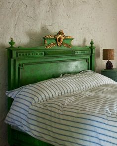 a bed with a green headboard and striped comforter in a room that has white walls