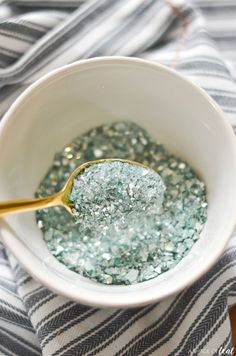 a white bowl filled with blue and silver glitter next to a gold spoon on top of a striped table cloth