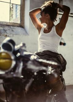 a woman sitting on top of a motorcycle in a garage with her hand on her head