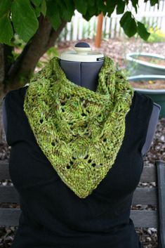 a woman wearing a green knitted scarf on top of a wooden bench next to a tree