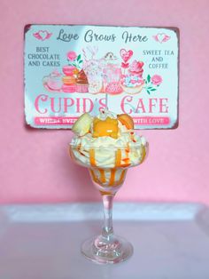 an ice cream sundae in a glass on a pink table with a sign above it