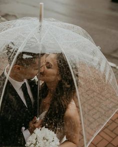 a bride and groom kissing under an umbrella in the rain on their wedding day,