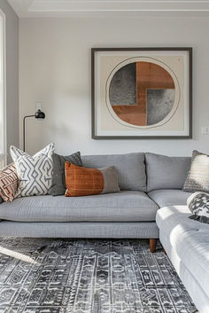 a living room with gray couches and pillows on top of the rug in front of a large window