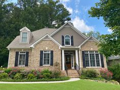 a brick house with black shutters on the front and side windows, surrounded by lush greenery