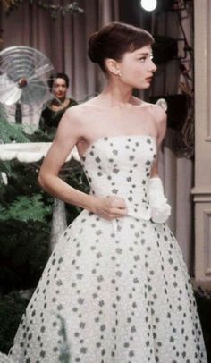 a woman in a white and black dress standing next to a christmas tree with people behind her