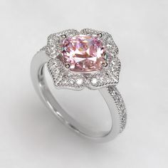 The Platinum Plated Sterling Silver Ring, Cushion Super Light Pink CZ Stone Milgrain Vintage 2 carat Engagement Ring, Pink Diamond Simulant Ring Cocktail Ring (Size 5 to 9) is nothing short of breathtaking. With its vintage-style vibe, it showcases an eye-catching light pink cushion cut cubic zirconia encircled by sparkling round cut accents set in milgrain edge finish petals being formed a heart shape. It would be a sensation at a garden party and a lovely complement to your little black dress Classic Pink Cluster Ring With Center Stone, Classic Pink Cluster Ring With Halo Setting, Classic Pink Cluster Ring With Prong Setting, Classic Pink Halo Ring With Gemstone, Classic Pink Gemstone Halo Ring, Pink Diamond Promise Ring With Halo Design, Formal Pink Halo Design Ring, Elegant Pink Flower Ring For Anniversary, Classic Pink Jewelry For Promise