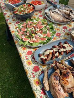 a table topped with lots of food on top of a grass covered field next to trees