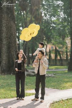 a woman holding up a yellow balloon with a child on her shoulders and another person standing next to her