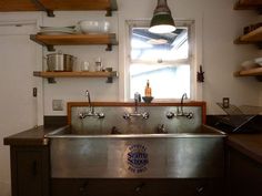 a stainless steel kitchen sink with two faucets on the side and open shelves above it