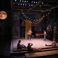 people sitting on the floor in front of a stage with lights strung from above them