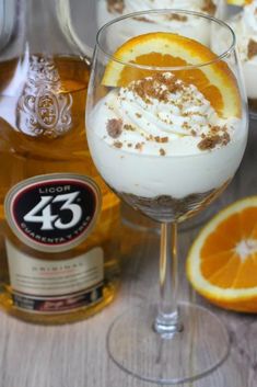 an orange slice is garnished with whipped cream in a wine glass next to some liquor bottles