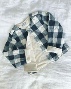 two shirts laying on top of a bed next to each other, one in black and white checkered