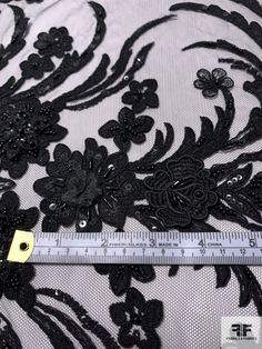 a ruler is measuring the length of a black lace fabric with flowers and leaves on it