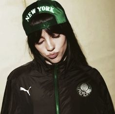 a woman wearing a black jacket and green hat with the words new york on it