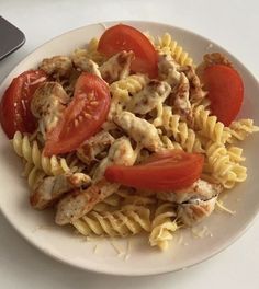 a white plate topped with pasta covered in chicken and tomato slices next to a laptop