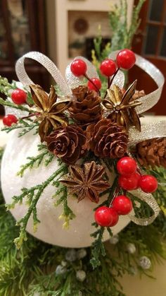 a white pumpkin decorated with pine cones, berries and evergreen needles is sitting on a table