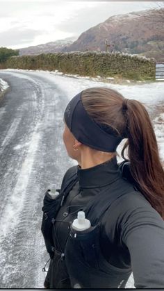 a woman standing on the side of a snow covered road with her back to the camera