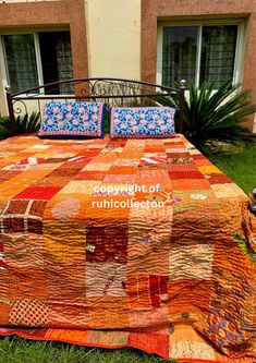 a quilted bed sitting on top of a lush green field next to a building