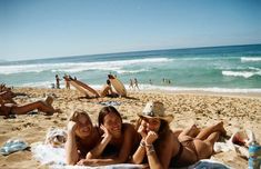 two women laying on the beach with their arms around each other and smiling at the camera