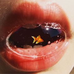 a person's lips with water and a goldfish floating in the lip area