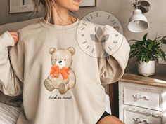 Women's Cute Teddy Bear Halloween Sweatshirt - Cozy Fall Fashion, women's Halloween sweatshirt, cute fall sweatshirt, teddy bear Halloween top, trick or treat sweater, autumn fashion, cozy fall clothing, women's fall sweatshirt. Get ready for the spooky season with our adorable Women's Cute Teddy Bear Halloween Sweatshirt! This light beige sweatshirt features a charming teddy bear holding a tiny orange pumpkin, complete with a playful "trick or treat" slogan. Perfect for adding a touch of whimsy Fall Bear Print Crew Neck Top, Bear Print Crew Neck Top For Fall, Cute Fall Loungewear Sweatshirt, Beige Sweatshirt, Bear Halloween, Halloween Top, Sweater Autumn, Fall Clothing, Sweatshirt Cute