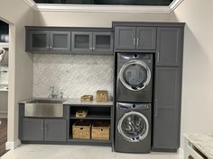 a washer and dryer in a kitchen with gray cabinetry, stainless steel appliances