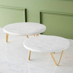 two white marble tables with gold legs on a table top in front of a green wall