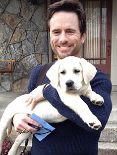 a man holding a white puppy in his arms and smiling at the camera while sitting on some steps