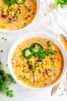 two white bowls filled with soup and garnished with cilantro, red onion, jalapeno peppers