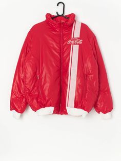 Vintage rare Coca Cola puffer jacket in cherry red. This jacket is official merch from Coca Cola and is a really rare piece to get your hand on!  The jacket has the Coca Cola logo on the left chest with white racing lines and features two front hand pockets with zip closure and a stretchy white hem. Made from a soft, lightweight material.  Our recommended size: Large  Label says: XL  Condition: Very good Material: 100% nylon  Measurements in inches: Pit to pit: 24 Shoulders: 20.5 Front length: 2 Retro Red Hooded Outerwear, Red 90s Style Streetwear Outerwear, 90s Red Outerwear For Streetwear, Red 90s Style Outerwear For Streetwear, Casual Red Puffer Jacket For Streetwear, Sporty Red Hooded Puffer Jacket, Red Outerwear With Padded Collar For Streetwear, Red Padded Collar Outerwear For Streetwear, Red Puffer Outerwear For Streetwear