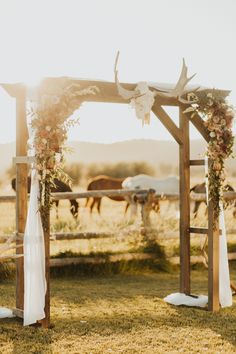 an outdoor wedding ceremony setup with flowers and greenery on the arch, horses in the background