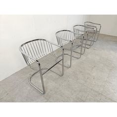 three metal chairs sitting next to each other in a room with concrete flooring and white walls