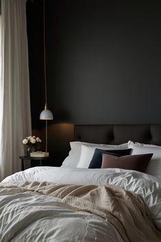 a bed with white sheets and pillows next to a window in a dark colored room