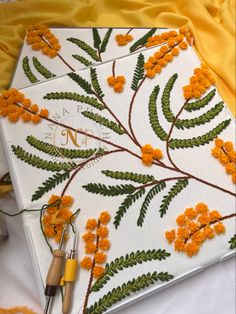 an embroidery project with orange flowers and green leaves on white fabric, next to scissors and thread