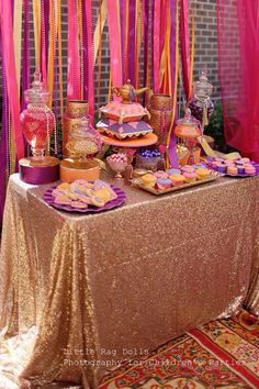 a table topped with lots of desserts next to pink drapes and streamers