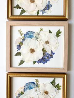 two framed pictures with white and blue flowers on the wall next to each other in gold frames