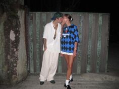 two people standing next to each other in front of a wooden fence at night time