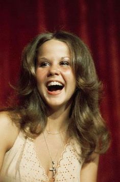 a woman laughing while standing in front of a red curtain