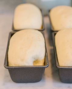 four loafs of bread sitting in pans on a counter top, ready to be baked