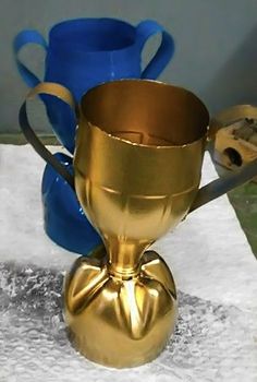 two shiny gold cups sitting on top of a white table cloth next to blue vases