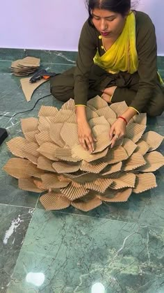 a woman is sitting on the floor working on some paper flowers that are made out of cardboard